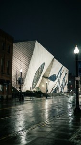 一座夜晚亮燈的現代建築，雨濕的街道反射著路燈。