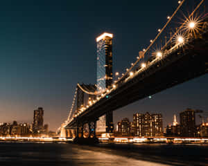 布魯克林大橋在夜晚亮起燈光，城市燈光倒映在水面上。