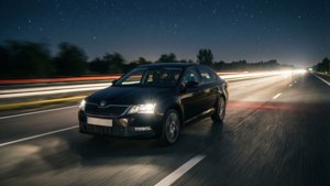 黑色汽車在星光燦爛的夜晚高速公路上快速行駛，帶有光跡。