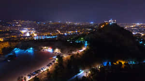 城市夜間鳥瞰圖，有燈火通明的山頂堡壘和閃閃發光的海濱。 — 夜晚 GIF 壁紙