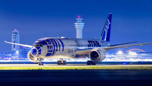 夜間機場停機坪上的R2-D2主題飛機，背景有控制塔。