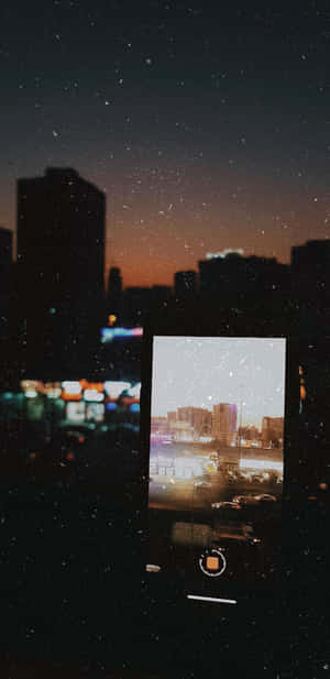 手機屏幕顯示黃昏時分的城市，雪花在繁星夜空下飄落。 — 月色夜空 壁紙