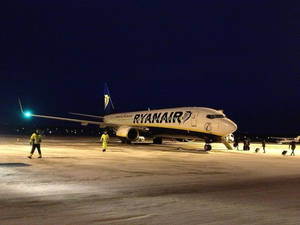 夜間積雪跑道上的瑞安航空飛機，地勤人員在附近行走。