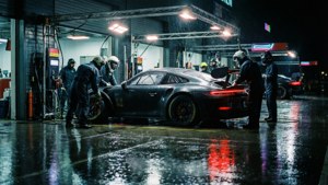 機械師團隊在夜間潮濕的車房中維修一輛黑色賽車。