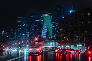 夜晚城市街道，發光的建築物和潮濕的人行道反射汽車燈光。 — 夜景城市 壁紙