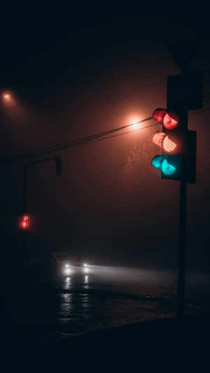 交通燈在夜晚的霧濕街道上閃爍紅綠光，伴隨著車頭燈。