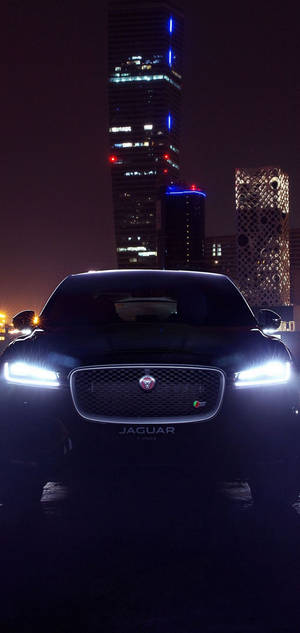 黑色Jaguar F-Pace夜間停車，背後是燈火通明的城市建築。