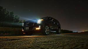 黑色Cadillac SUV在星空下的碎石路上亮著車頭燈。