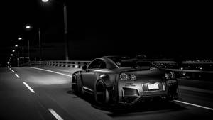 黑色跑車在夜間高速公路上高速行駛，帶有動態模糊效果。 — 天際線 壁紙