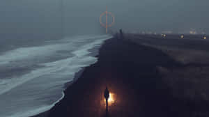 一個人在黑暗的海灘上走向霧氣瀰漫的遠方發光圓圈。 — 夜晚 GIF 壁紙