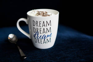 白色馬克杯有dream字樣和忌廉，深藍色布料上放有匙羹。