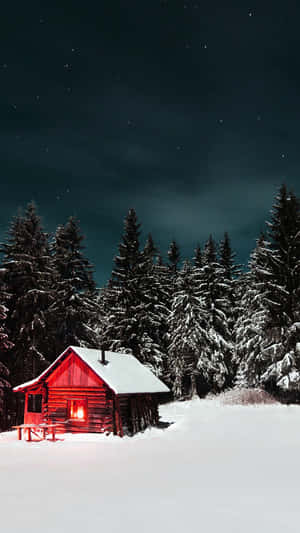 在繁星點點的夜空下，雪地森林中一間有亮著窗戶的紅色小屋。