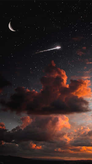 暮色中發光的橙色雲層上的新月和流星。