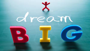 黑板上色彩繽紛的泡棉字母拼出BIG，黑板上有粉筆寫的dream字樣，上面有一個小小的紅色火柴人。