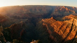 日出時的大峽谷，金色光線照亮紅色岩層。