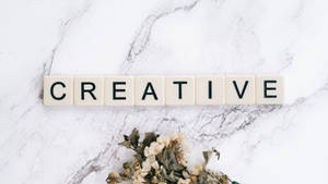 奶油色瓷磚在大理石上拼出creative，下方有乾花。 — 高解析度 壁紙
