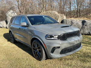 灰色 Dodge Durango SUV 停泊在戶外草地上，靠近大石頭和光禿禿的樹木。