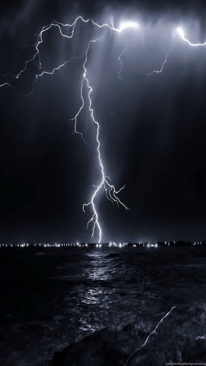 閃電劃過黑暗的海洋，地平線上可見城市燈光。