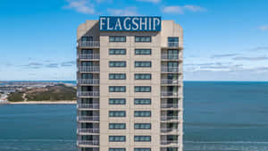 高嘅米色酒店塔樓帶有'FLAGSHIP'標誌，喺晴朗日子俯瞰海洋。 — 紐約市 壁紙