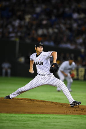 穿著條紋制服的棒球投手在夜間燈光下投球中。 — 日本 壁紙