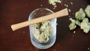 玻璃罐裝有大麻花蕾和一根捲好的大麻煙，放在木桌上。