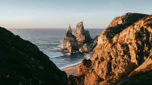 金色夕陽映照海岸懸崖和海蝕柱，海浪拍打沙灘。
