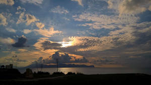 海洋上的夕陽，山巒輪廓和散落的雲彩。