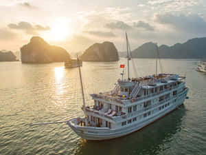白色郵輪在日落時分航行於有喀斯特島嶼的海灣。