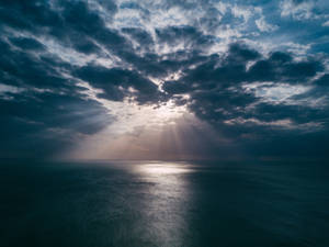 陽光穿透黃昏時分平靜海洋上空的烏雲。