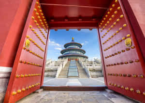 帶有金色門釘的紅色大門，在藍天下框住天壇。 — 廟宇 壁紙