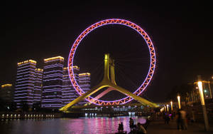 夜間城市景觀，發光的摩天輪和摩天大樓倒映在河中。