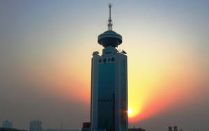 一座高塔在都市環境中矗立於色彩繽紛的日落天空下。 — 唐人街 GIF 壁紙