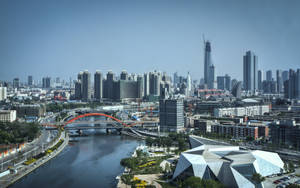 一座現代城市，在清澈的天空下，有一座橫跨河流的紅色橋樑和高樓大廈。