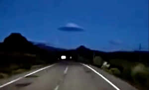黃昏時分模糊的道路，發光的UFO懸浮在山脈之上。