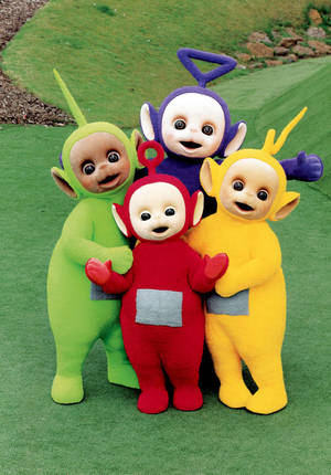 四個微笑的Teletubbies穿著色彩繽紛的服裝在草地上擁抱。 — 可愛卡通 壁紙
