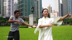 兩個人在城市公園中練習太極拳，身後有高樓大廈。
