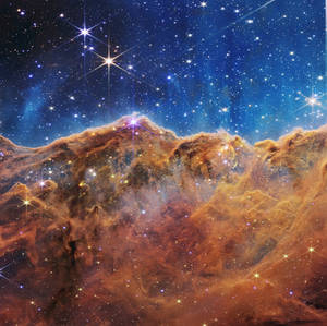 深藍色太空中充滿閃爍星星的發光橙色星雲雲朵。 — 太空 壁紙
