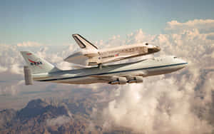 由改裝波音747運載的NASA太空穿梭機在雲層和山脈上空飛行。