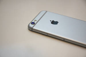 銀色 iPhone 6s 平放在純色表面上，顯示背面標誌和相機。