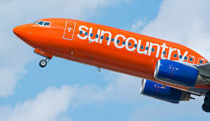 Sun Country Airlines飛機在晴朗藍天中飛行，伴有白雲。