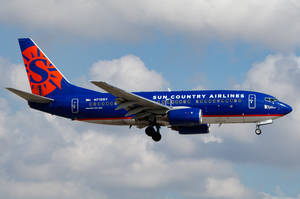 藍色和橙色的 Sun Country Airlines 噴射機在多雲的天空下著陸。