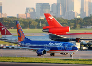 Sun Country Airlines 飛機在機場停機坪上，背景有日落時分的城市天際線。