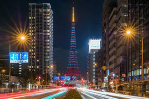 夜晚的東京塔被燈光照亮，周圍有汽車燈光軌跡和高樓大廈。