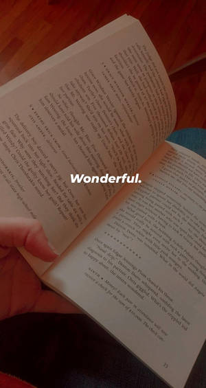 手拿著打開的書，木地板上覆蓋著「Wonderful」文字。 — 桌面美學 壁紙