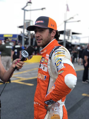 身穿橙色賽車服的NASCAR車手在賽道上接受Fox Sports記者採訪。