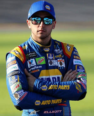 NASCAR車手身穿藍色賽車服，雙手交叉，站在草地上。