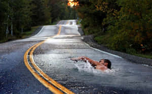 男子在被水淹沒的道路上游泳，周圍是秋日樹木，夕陽照耀