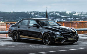 黑色 Mercedes-AMG E63 S 帶金色飾邊停泊在城市橋上。 — 酷車 壁紙