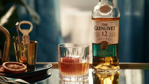 一瓶Glenlivet威士忌和一杯加冰的威士忌放在吧檯上，配有乾橙片。