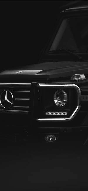 黑色 Mercedes G-Wagen 前格柵和頭燈在昏暗攝影棚燈光下的特寫。